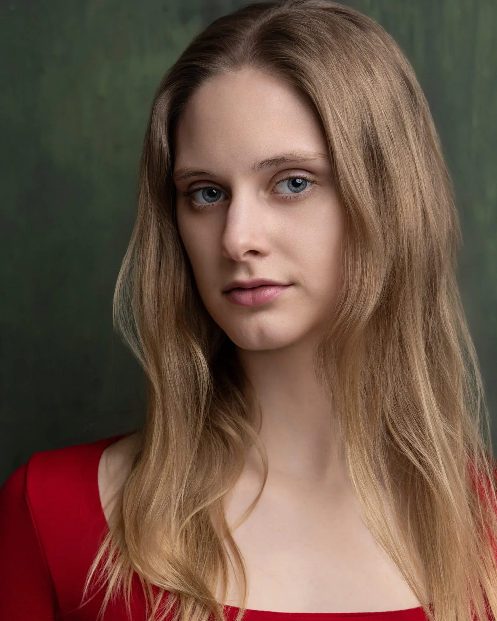 Cordelia June Reynolds, head and shoulders in a red top against a dark green backdrop, looking at the camera
