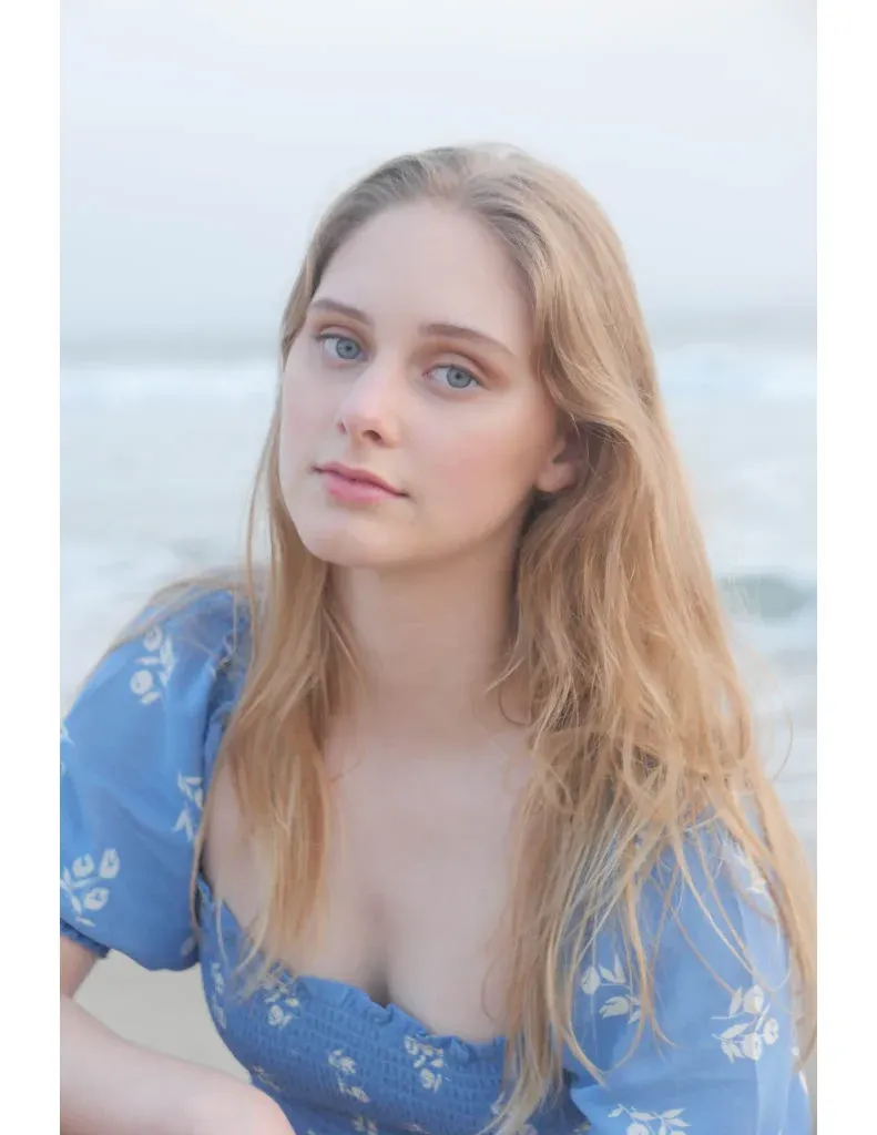 Cordelia June Reynolds by the sea in a blue floral dress, looking at the camera